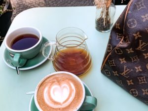 Louis Vuitton Bag Sitting On Table With Cup Of Coffees