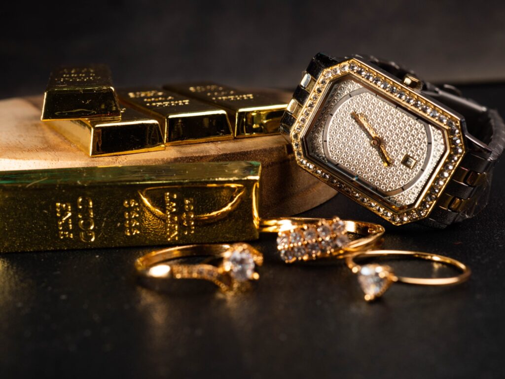 Gold bullion bars, a gold-tone wristwatch and rings on a dark surface
